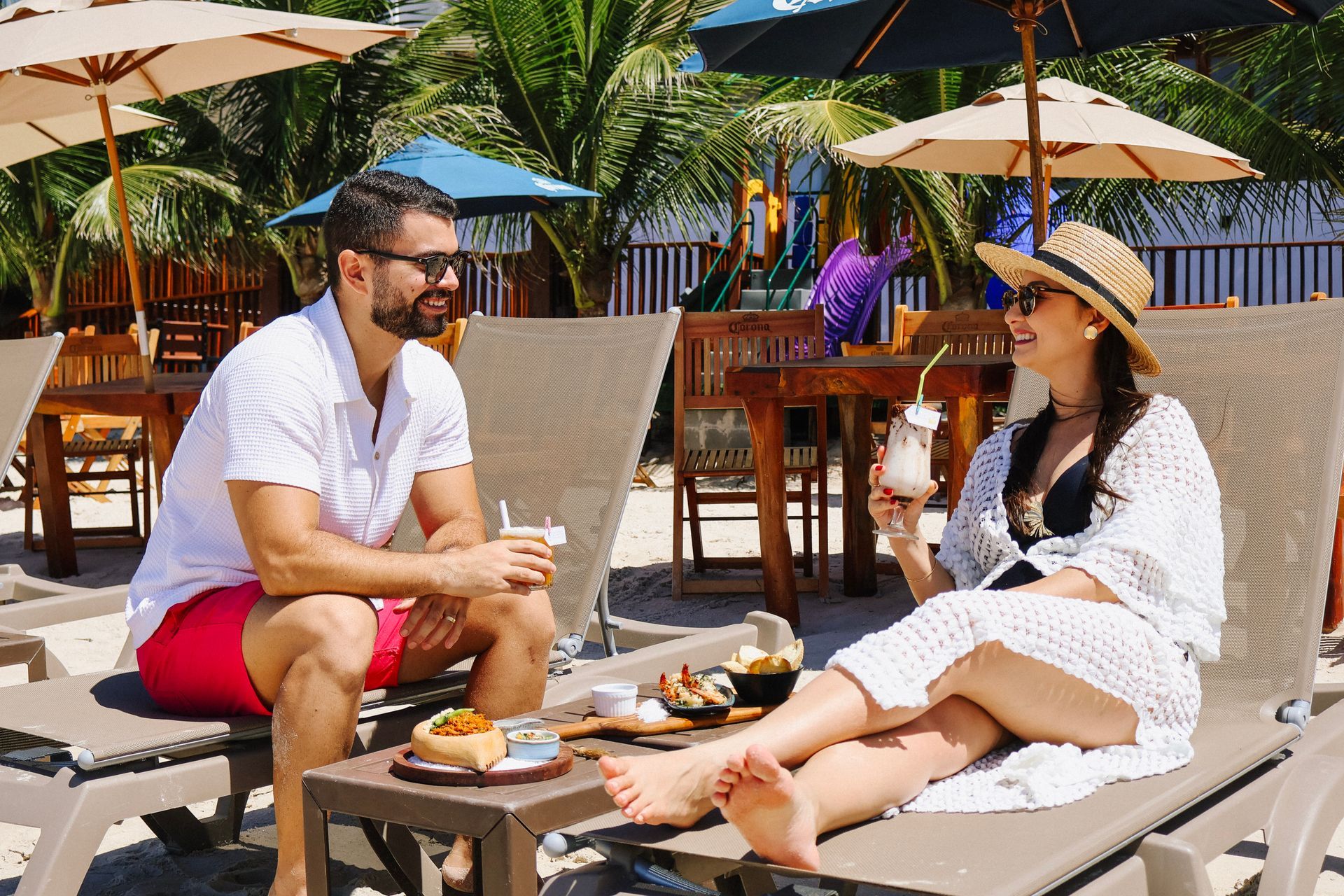 Um homem e uma mulher bebem cerveja em uma varanda com vista para o mar.