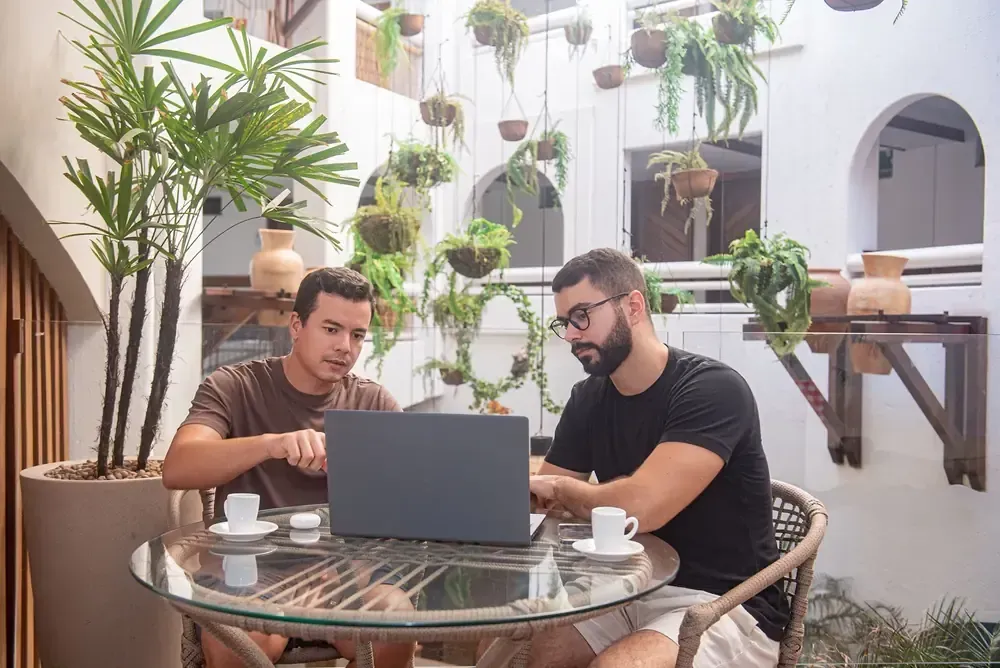 Dois homens estão apertando as mãos enquanto estão sentados em uma mesa com laptops.