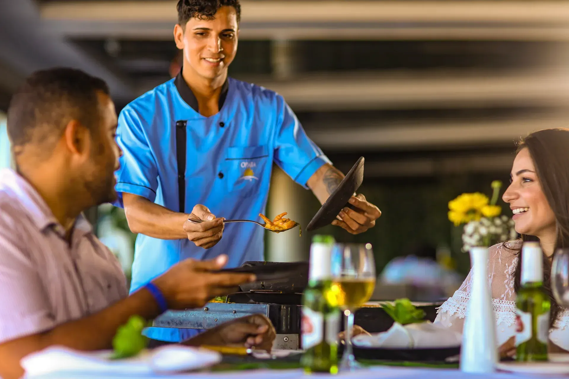 Um homem está servindo comida para uma mulher e um homem em um restaurante.