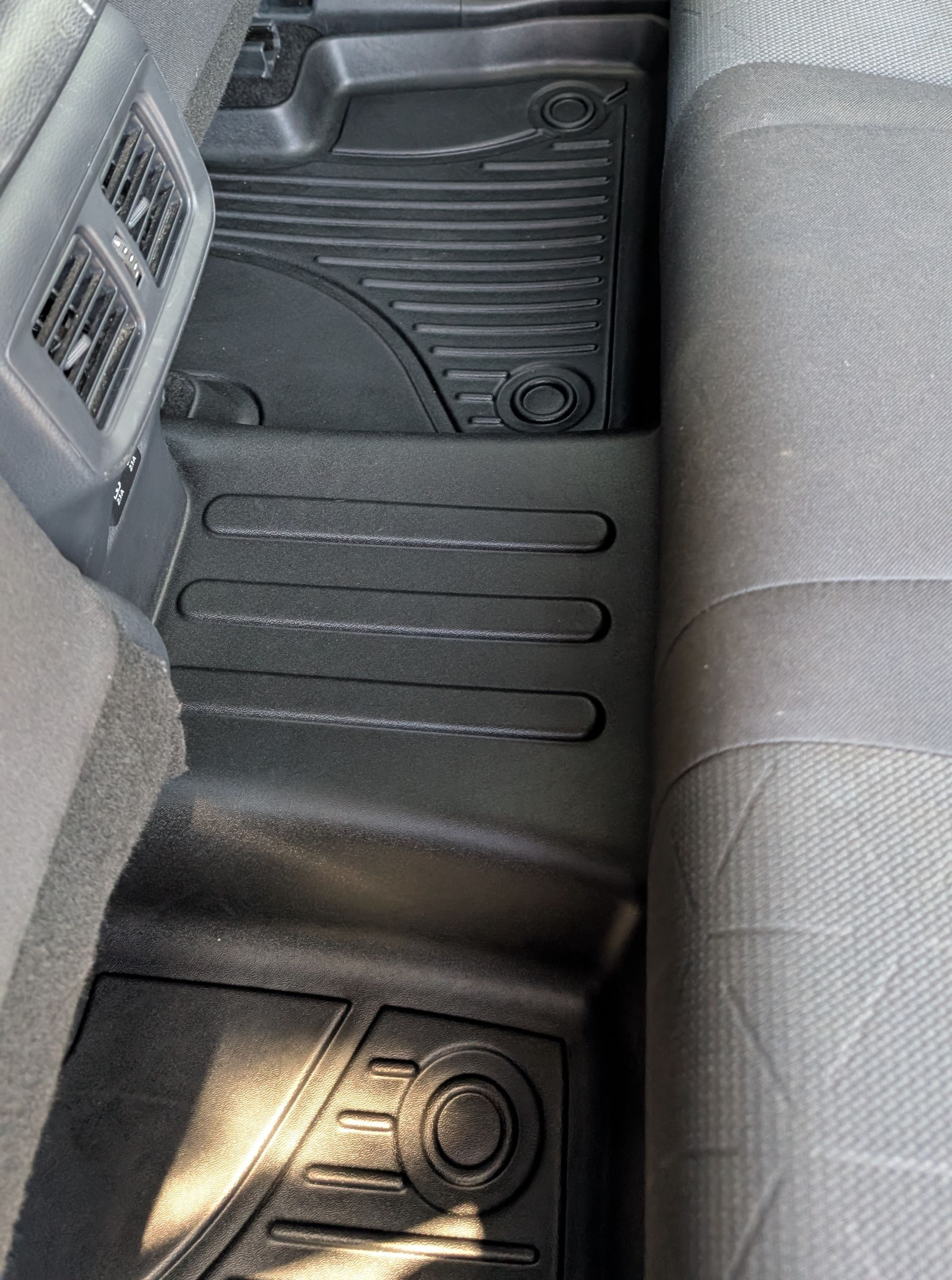 Rear seat footwell of a car with black rubber floor mats and gray patterned seats.