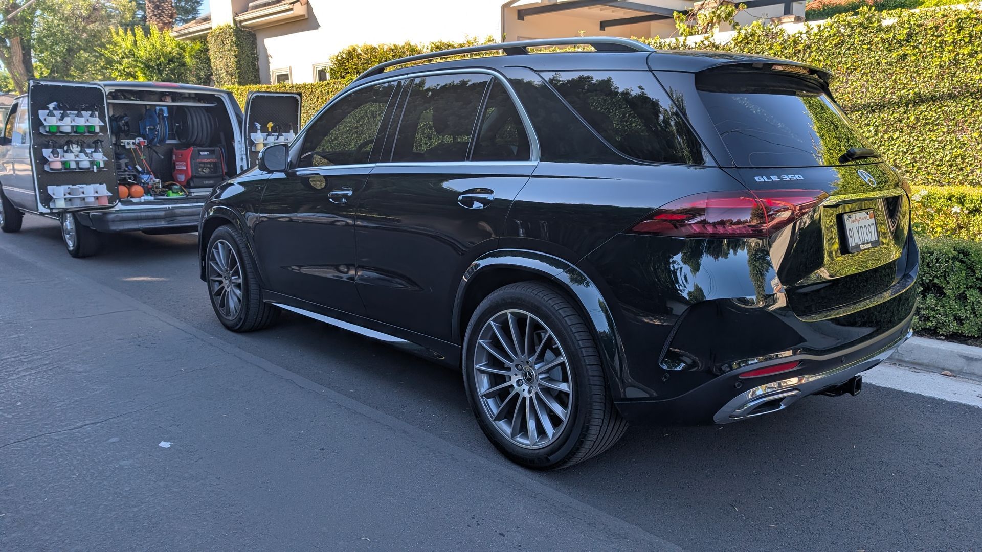 Black minivan parked on a street with a wrapped van behind it in daylight