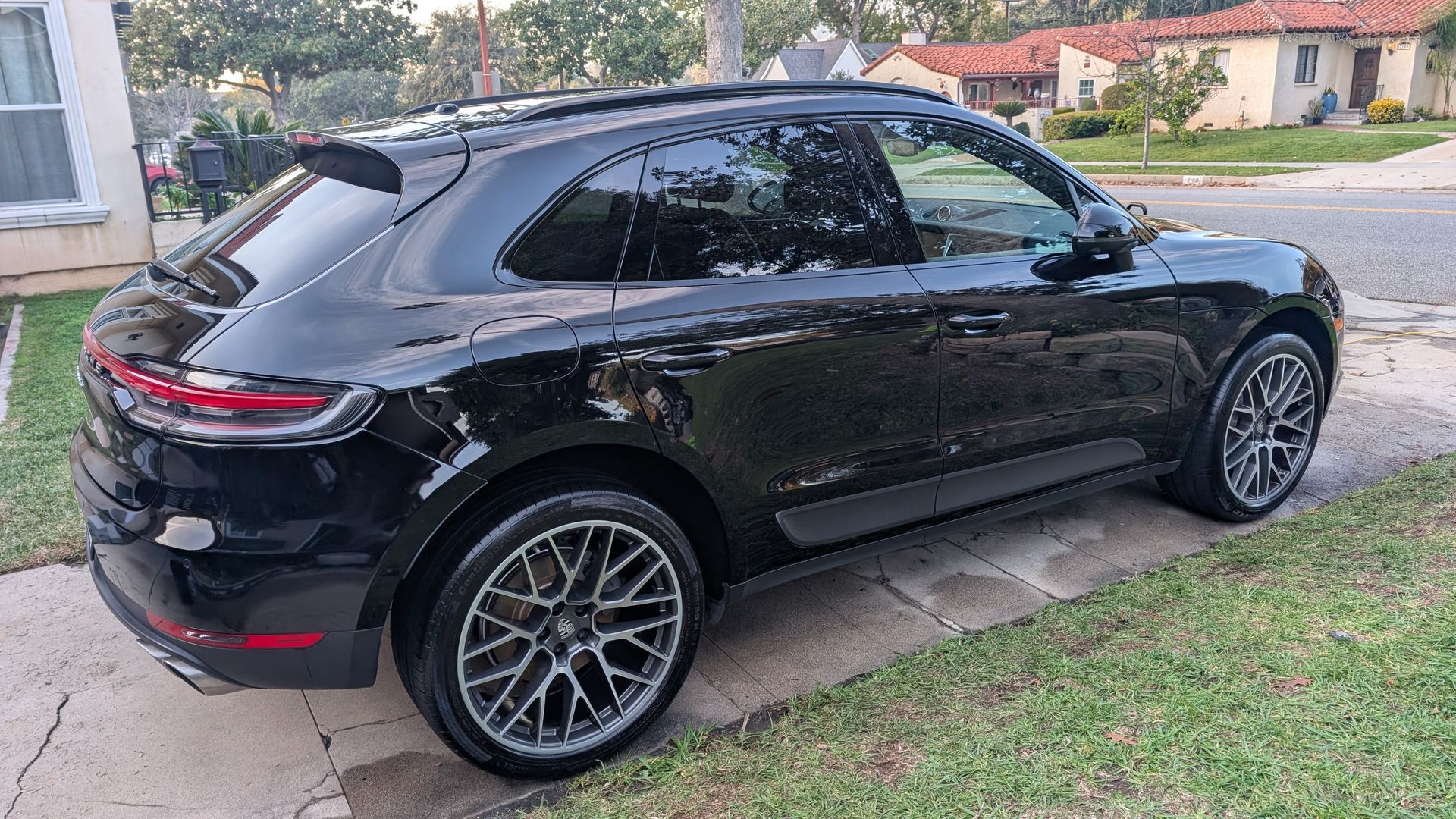 Black compact SUV parked on a driveway beside a grassy yard, rear three-quarter view.