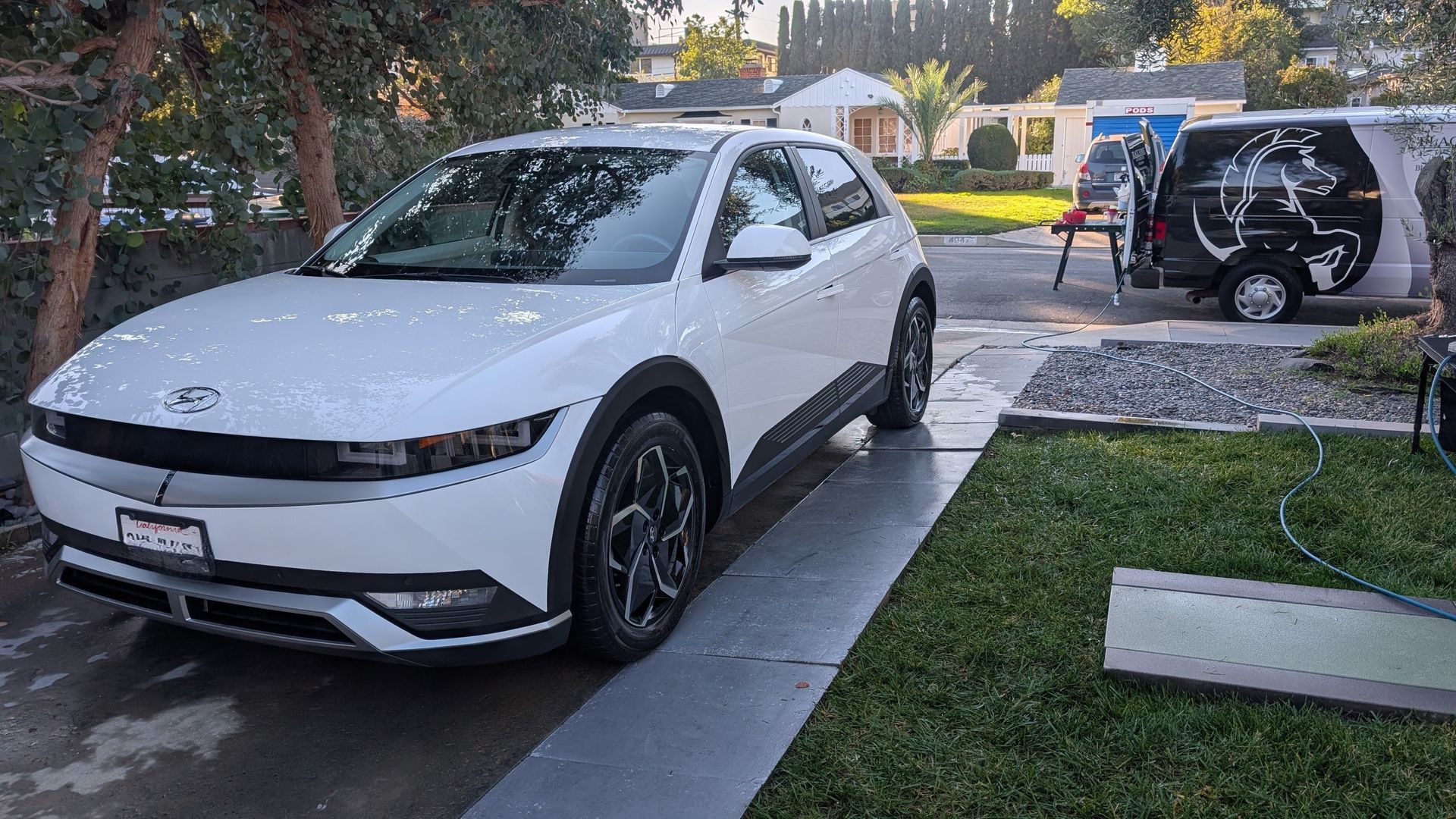 White hatchback in a driveway beside a lawn, with a black SUV parked in the background.