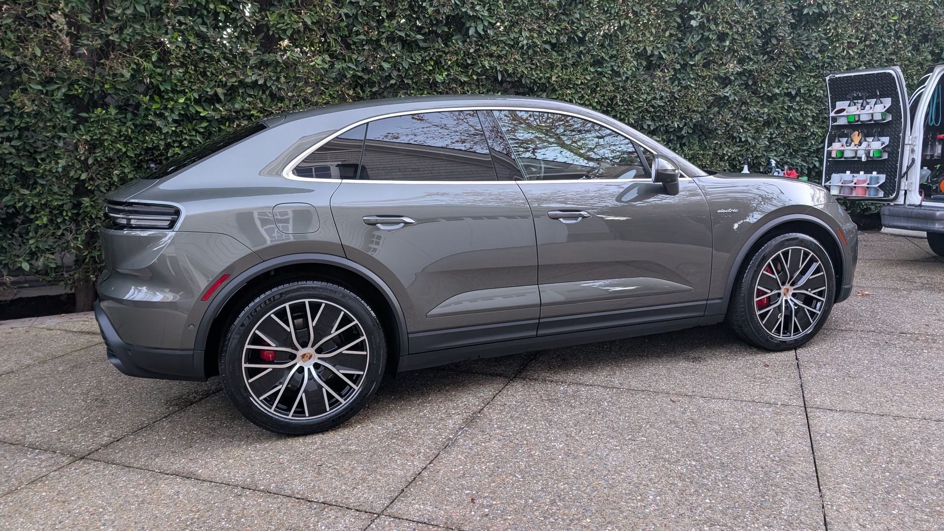 Gray electric SUV parked on a driveway beside trees and a charging station