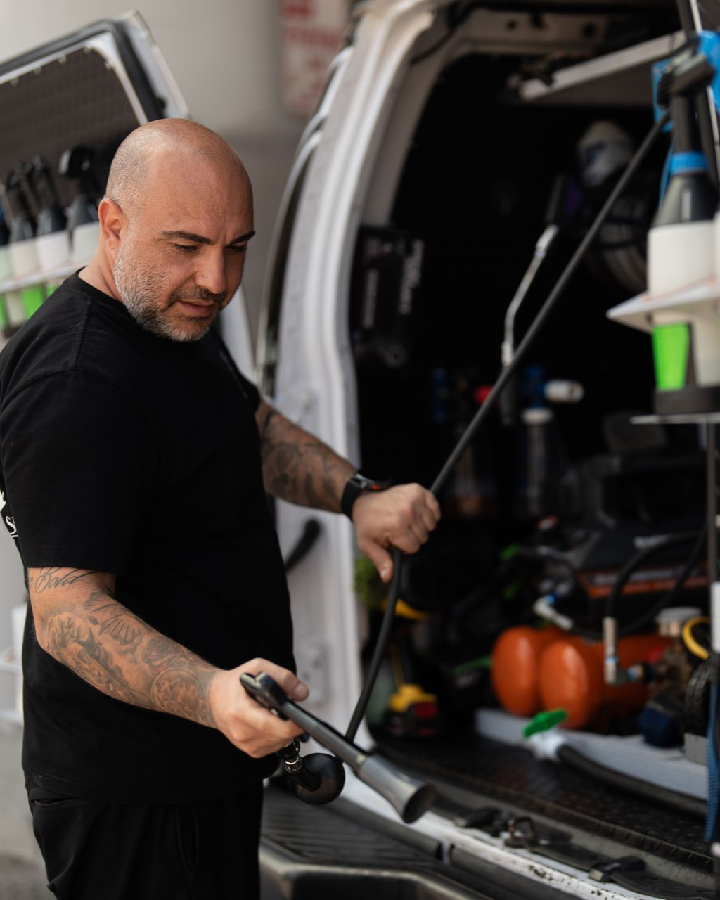Man spraying the open back of a van with cleaning equipment and bottles organized inside