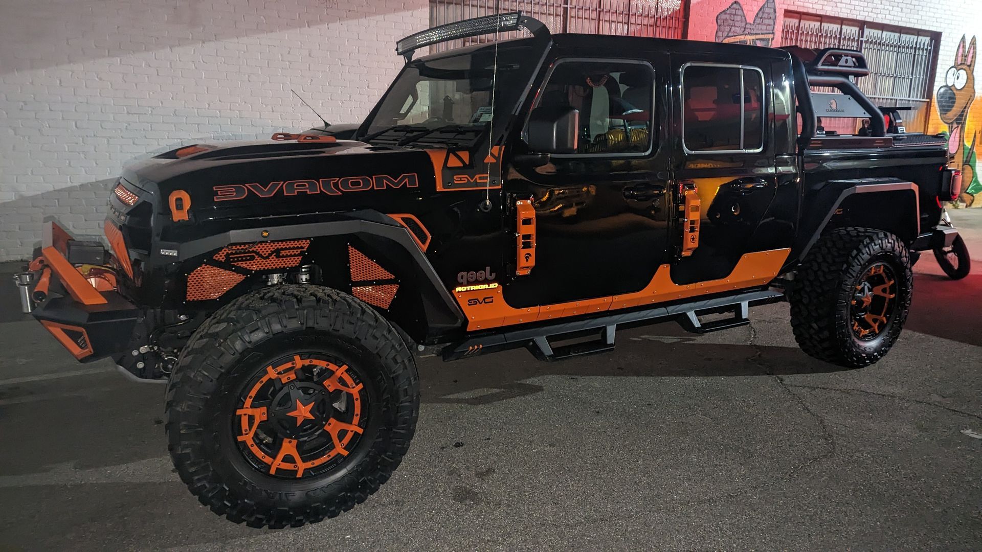 Black Jeep Wrangler with orange accents, lifted suspension, parked outdoors at night