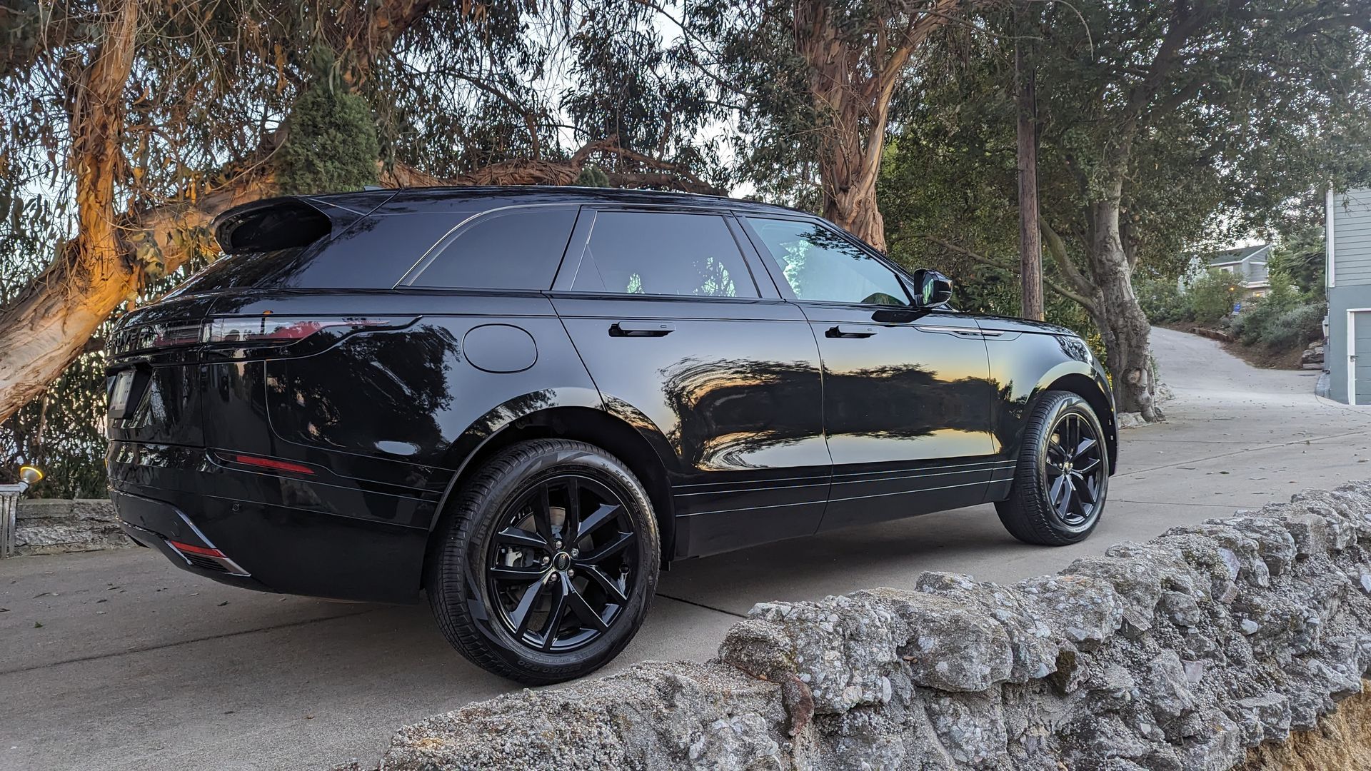 Black SUV parked on a roadside beside trees and a stone wall at sunset