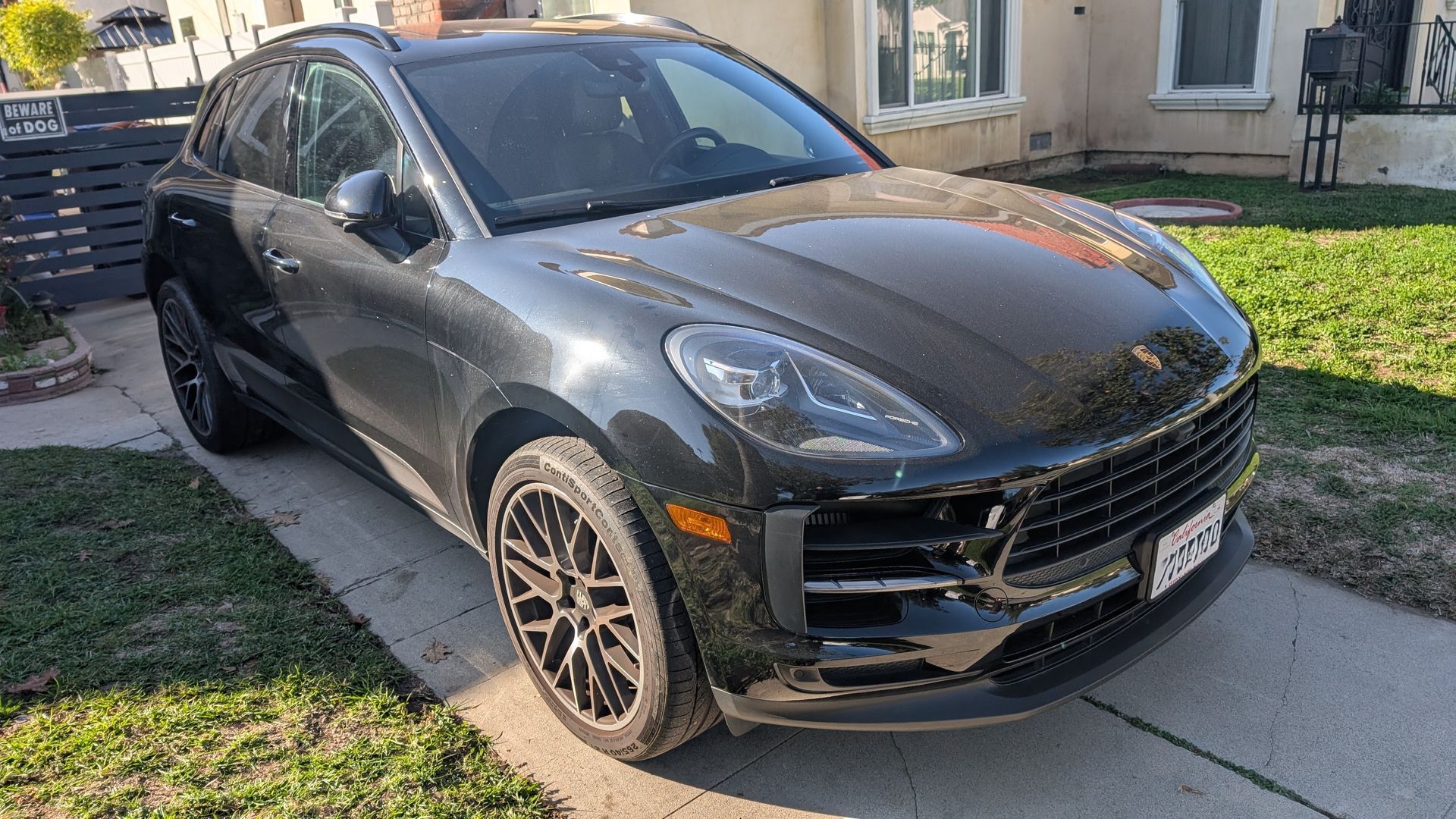 Dark gray Porsche SUV parked in a driveway beside a house, front-left view.