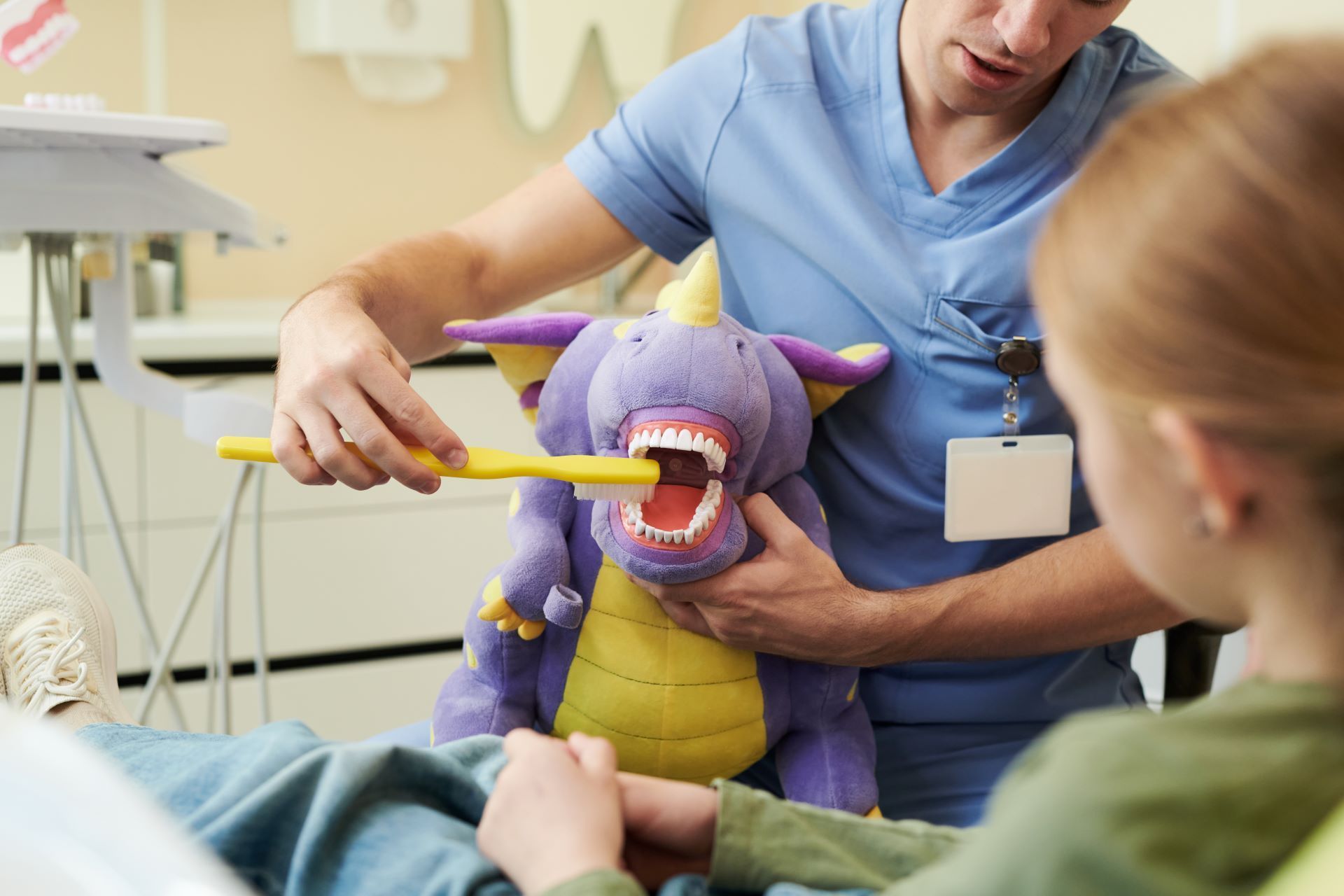 Dentist showing purple dinosaur puppet with open mouth to a child in a dental clinic