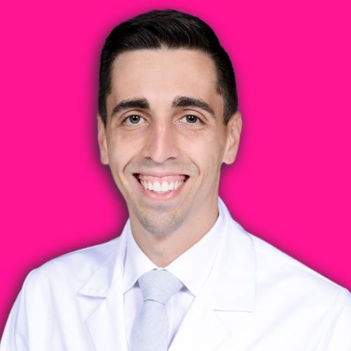 A smiling person in a white lab coat and tie, centered against a solid, bright pink background.