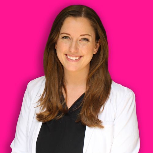 A person with long brown hair, wearing a white lab coat over a black shirt, smiling against a vibrant pink background.