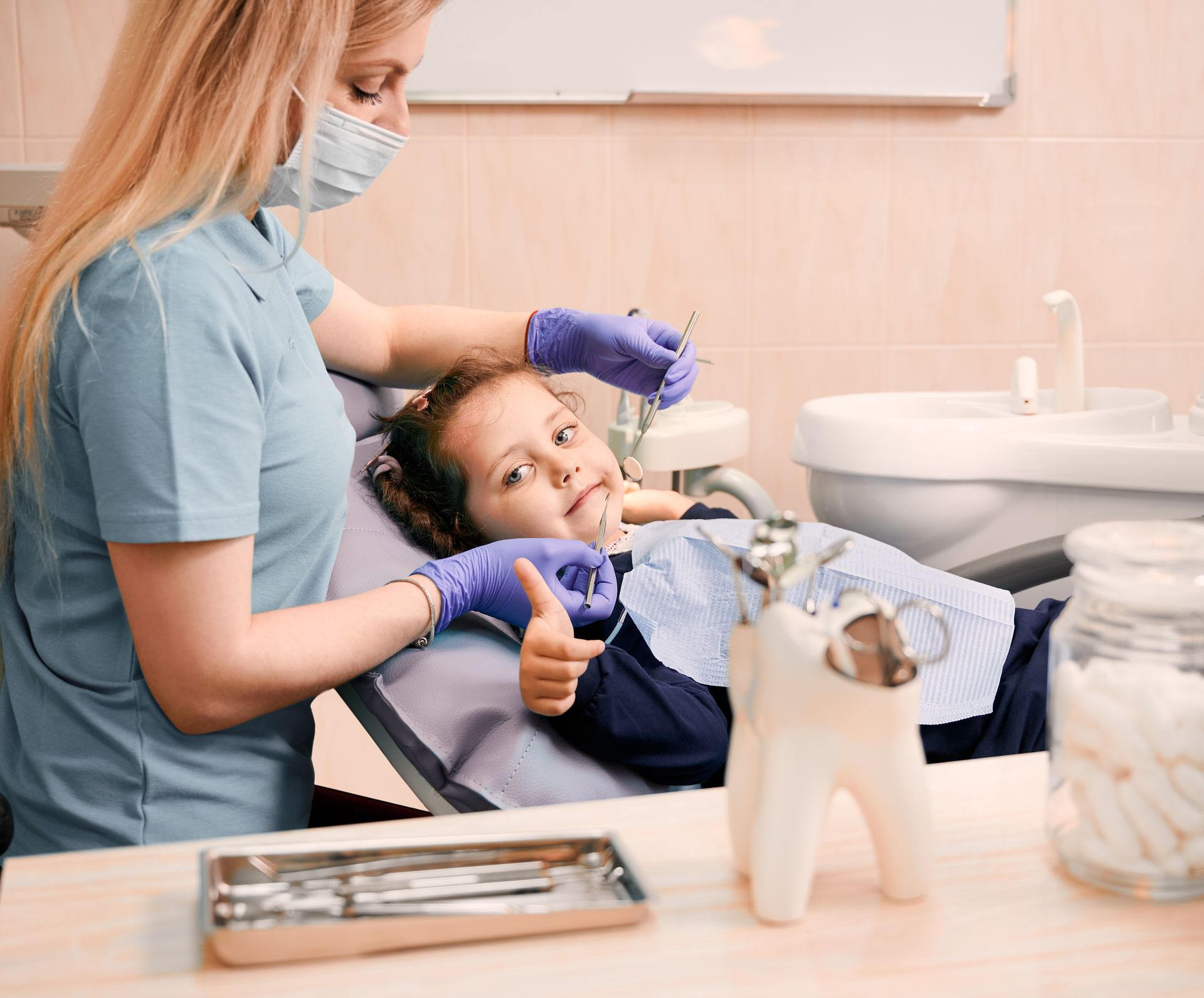 Dentist treating a child in a dental chair, with tools and sink visible in a bright clinic.