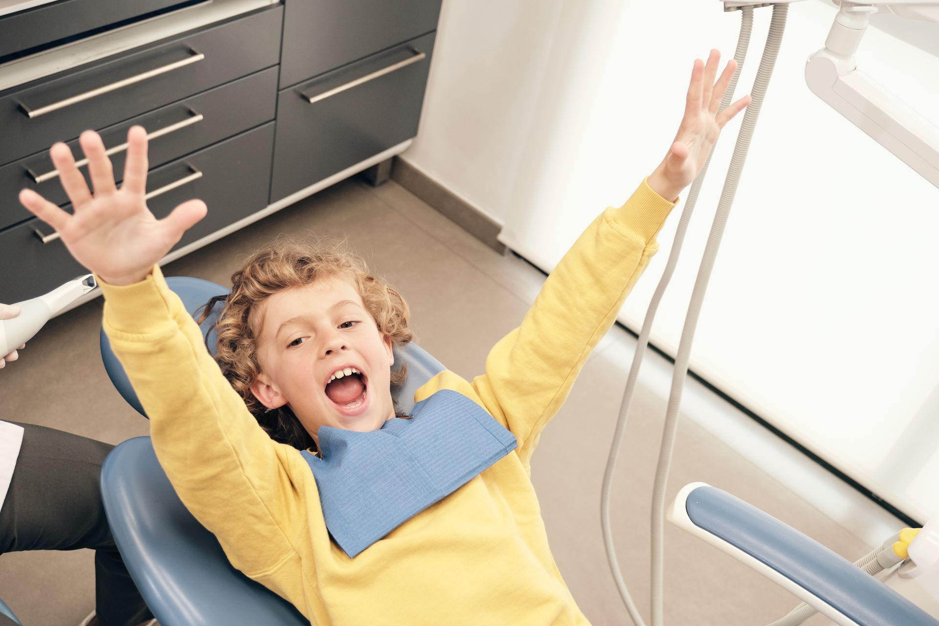 Child in a dental chair, smiling with arms raised during a dental visit