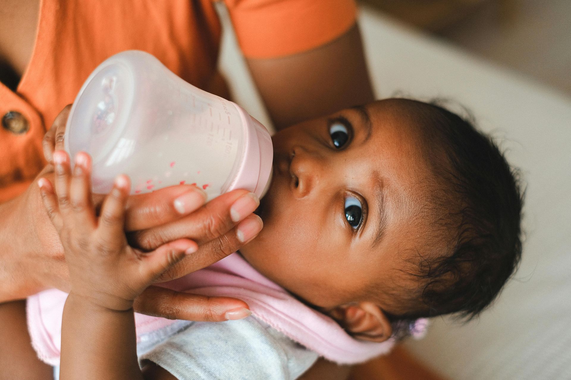 Adult feeding baby from a bottle on a couch