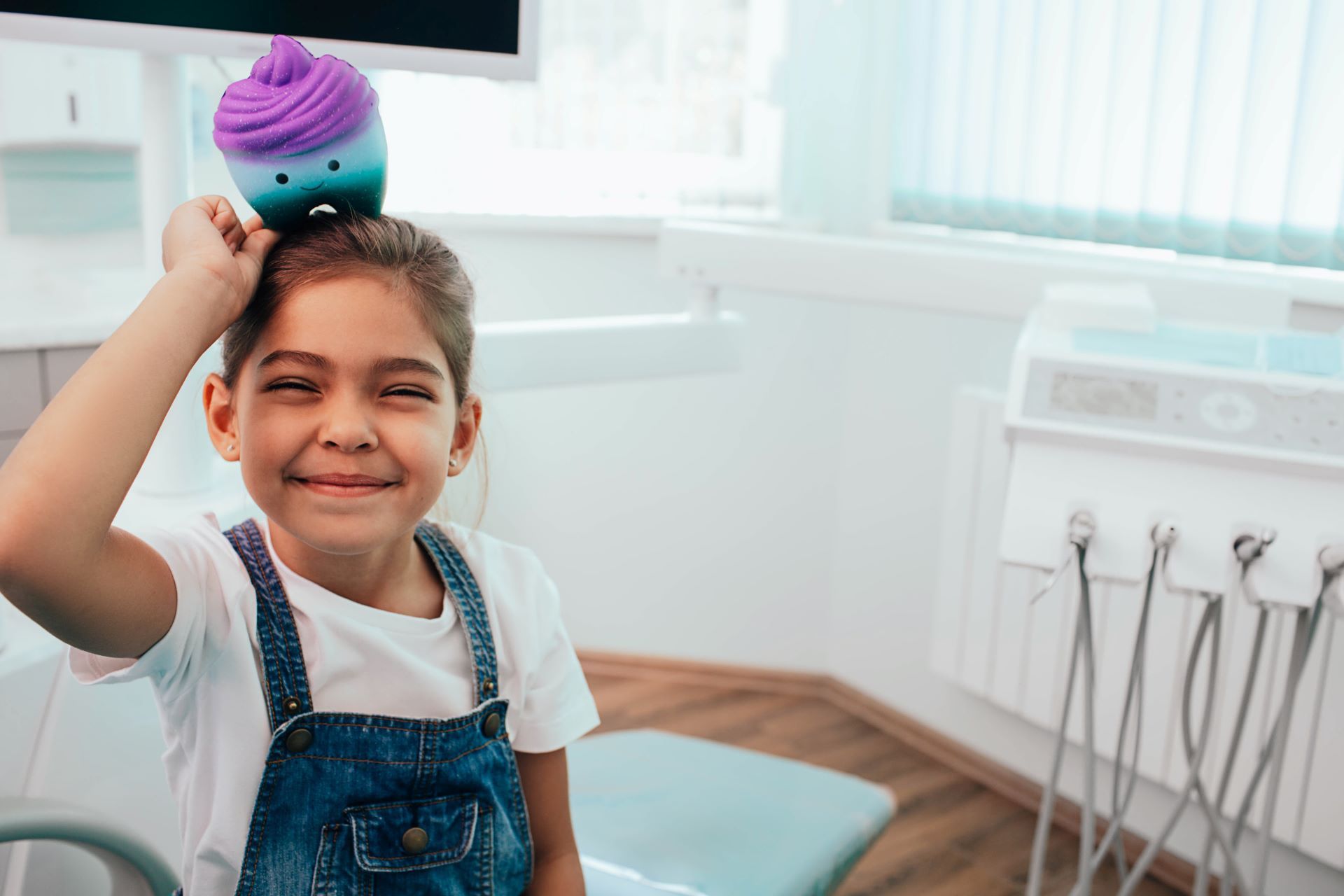 Child smiling in a dentist chair with a toy ice cream cone on their head in a bright clinic
