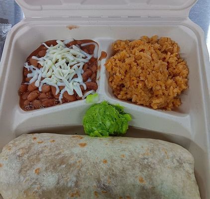 Burrito with sides of beans topped with cheese, rice, and guacamole in a takeout container.