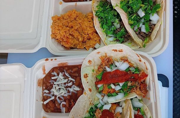 Tacos with rice and beans in takeout containers, topped with cilantro, onions, and salsa.