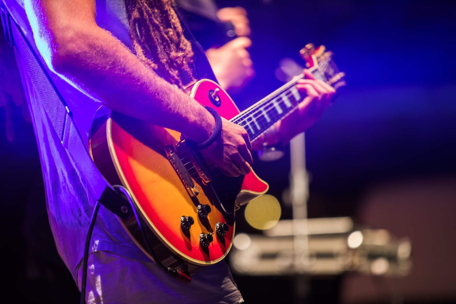 Guitarist performing on stage, holding red and yellow electric guitar.