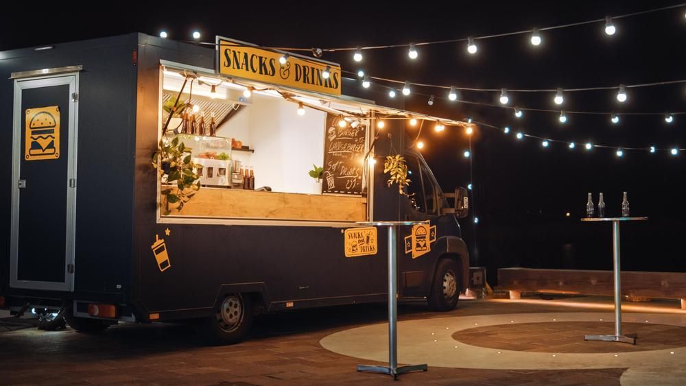 Food truck at night with string lights, serving snacks and drinks.
