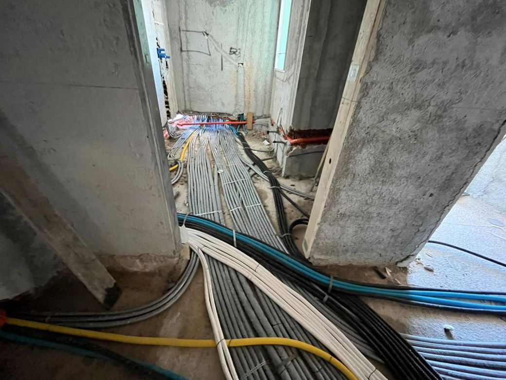 Il corridoio di un cantiere edile, con numerosi condotti e tubi elettrici posati sul pavimento di cemento grezzo.