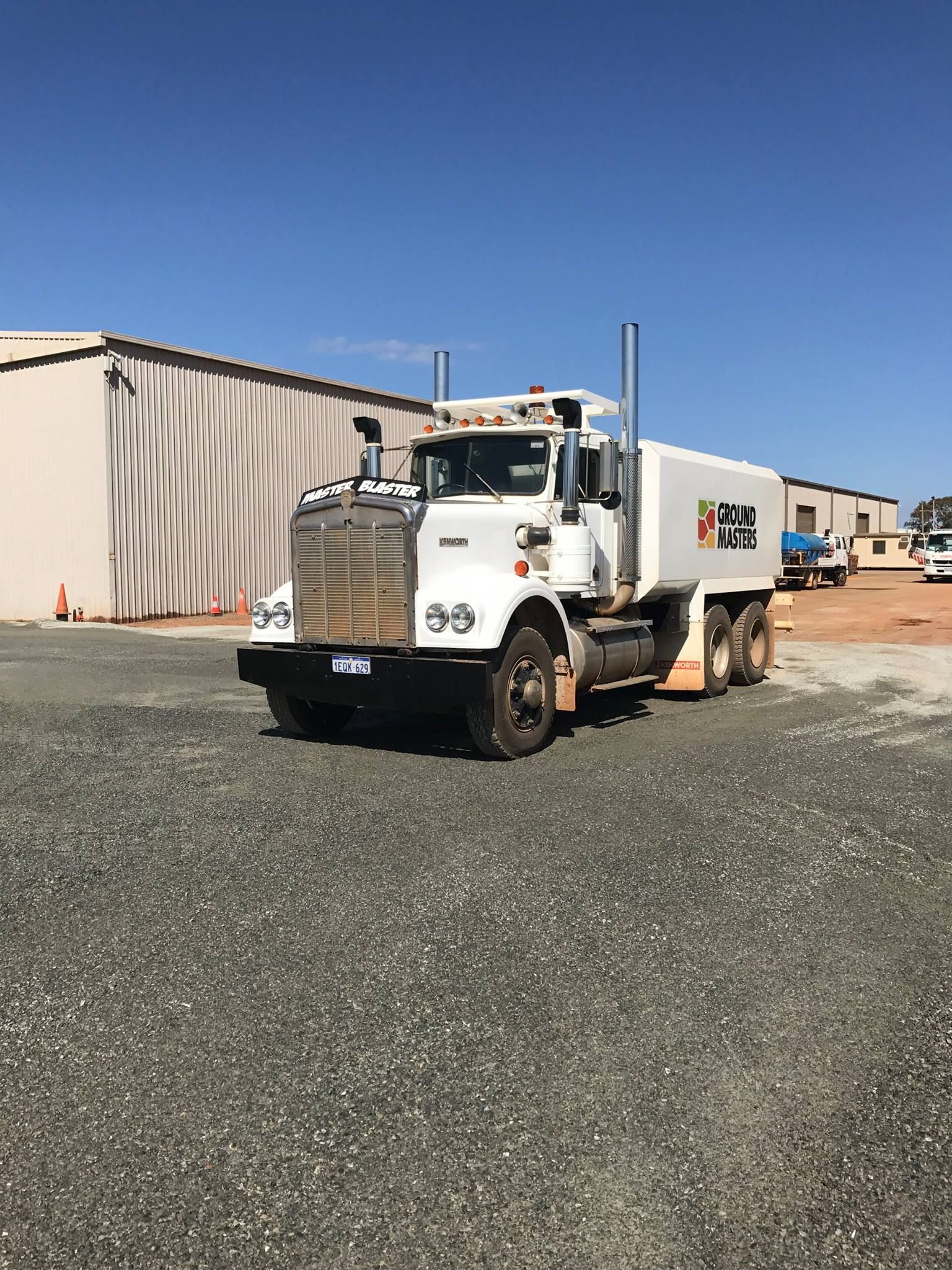 A white semi truck is parked in a gravel lot in front of a building.