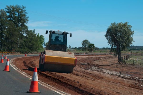 A road roller is working on the side of a road.
