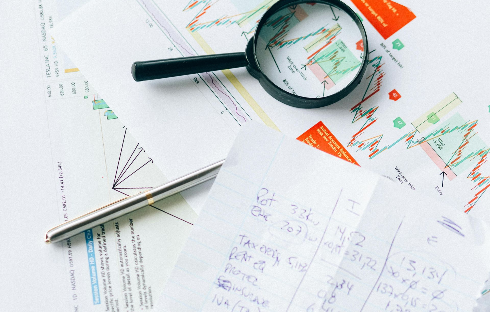 A magnifying glass rests on financial charts and a handwritten budget sheet, symbolizing business analysis and planning.