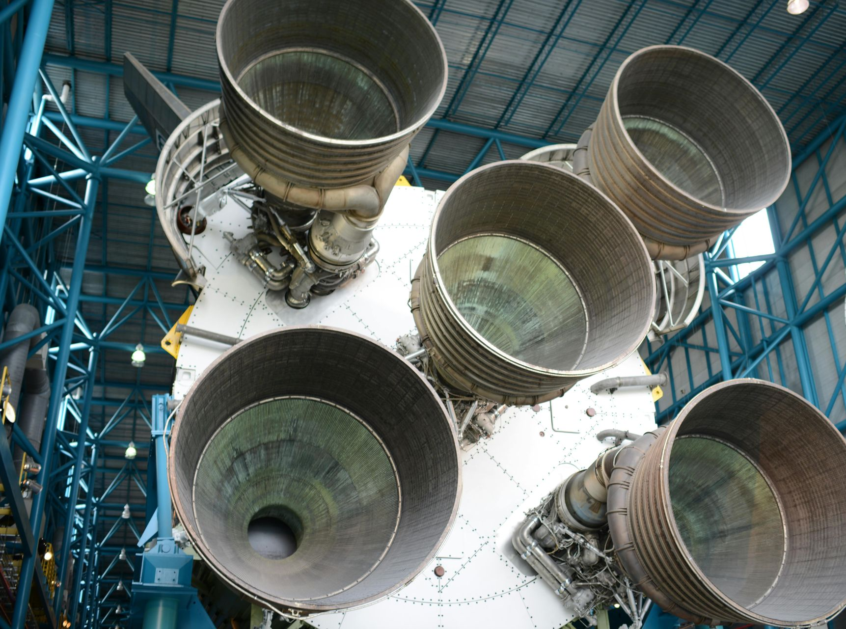 Five rocket engine nozzles on a spacecraft base in a hangar, viewed from below
