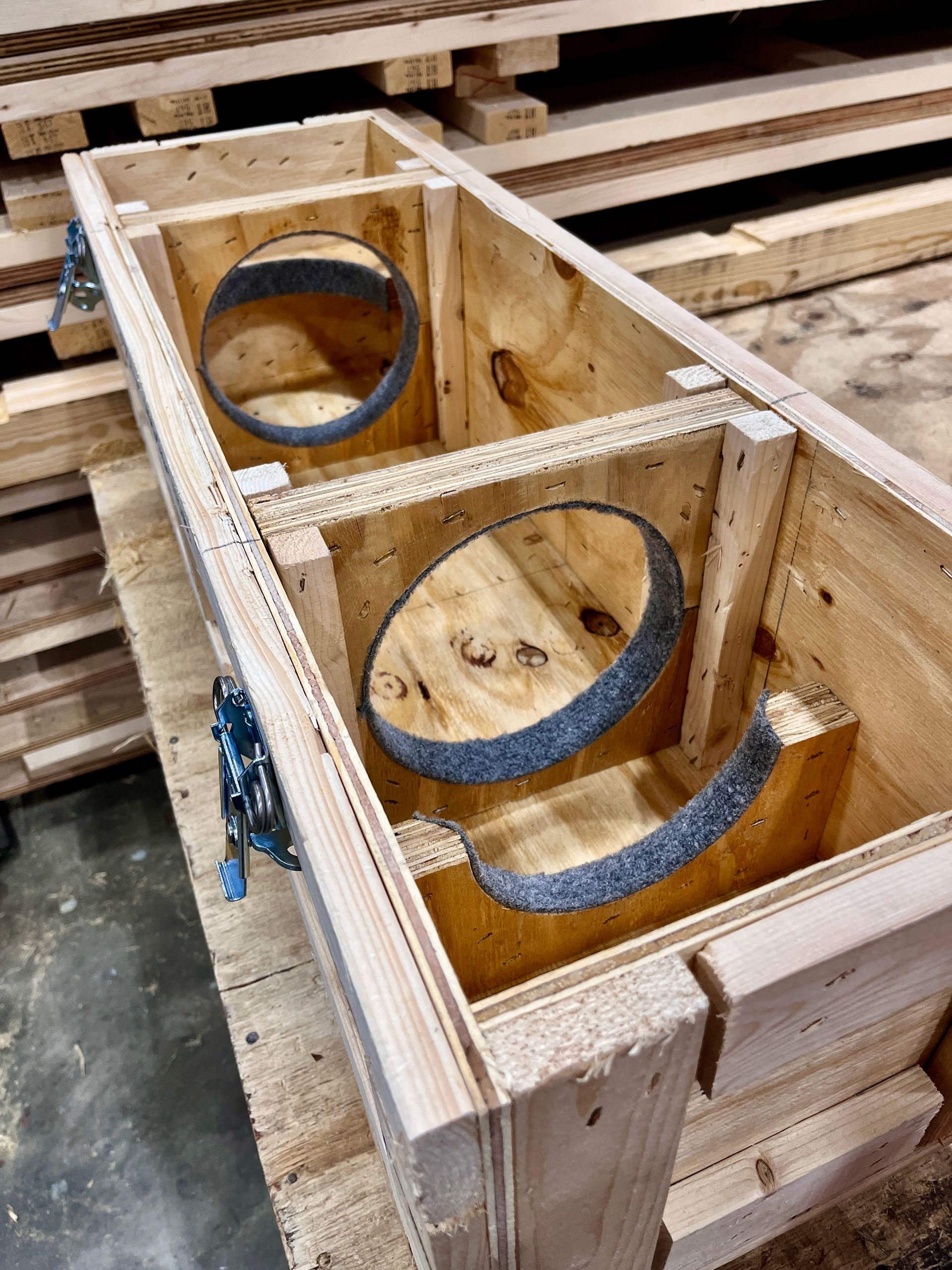 Wooden crate interior with two circular cutouts lined with gray padding, stacked on a pallet.