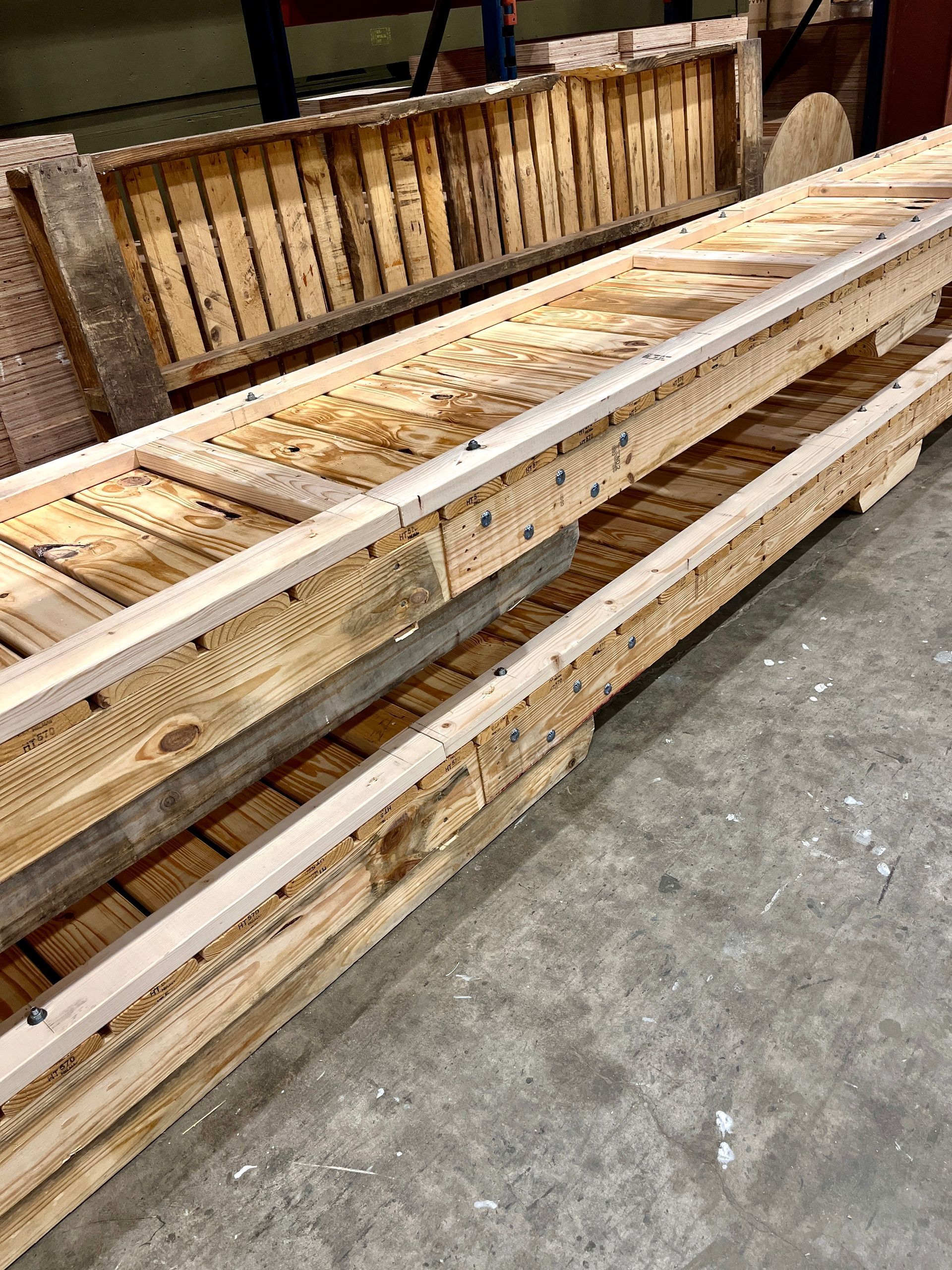 Stack of long wooden pallets in a warehouse setting.