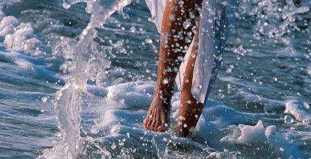 Eine Frau läuft barfuß im Wasser am Strand.