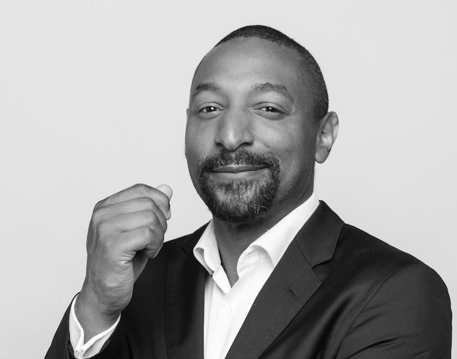 Man in suit, smiling, holding hand up near face, monochrome.