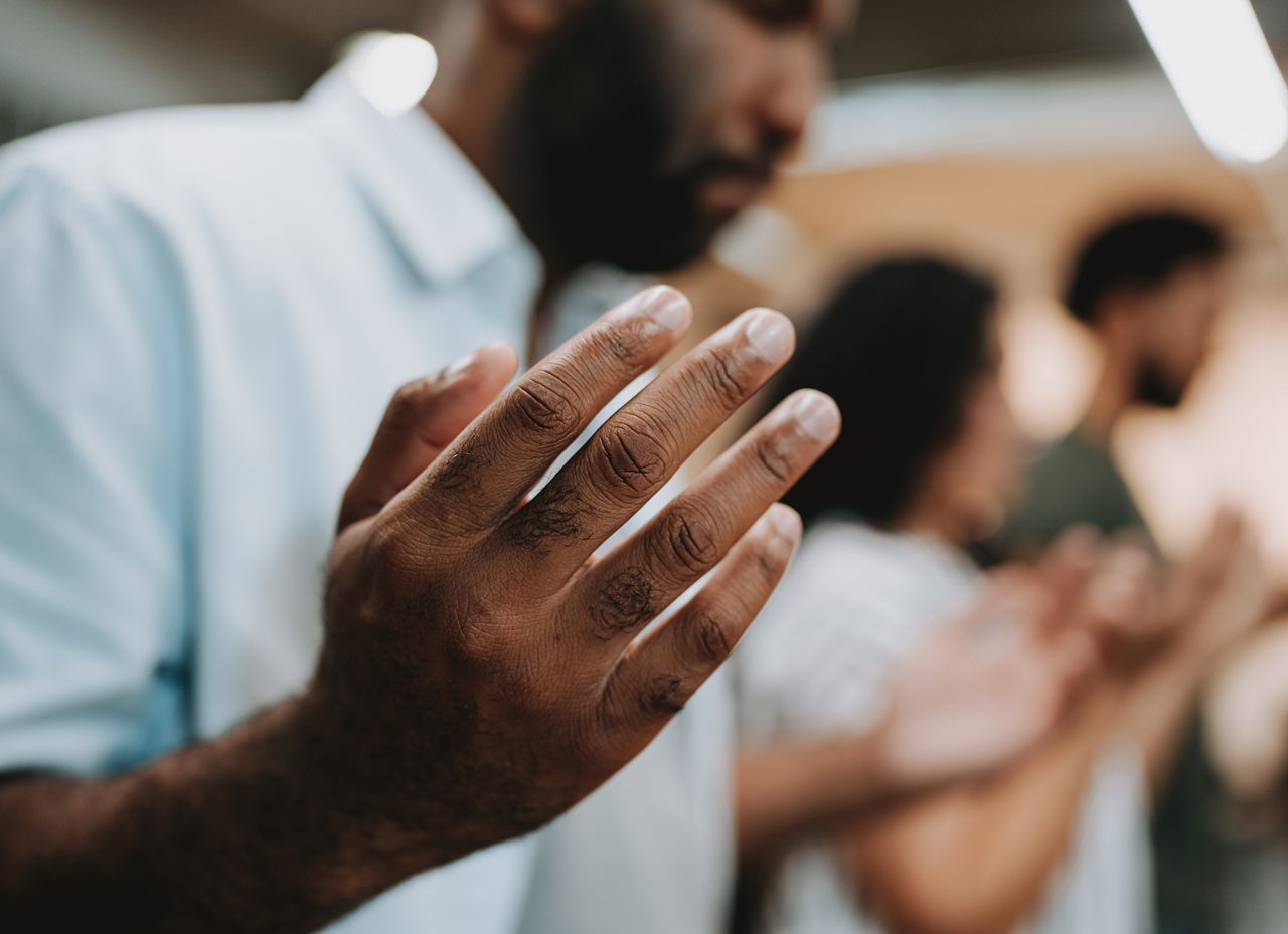 A man is praying with his hands outstretched in front of a group of people.