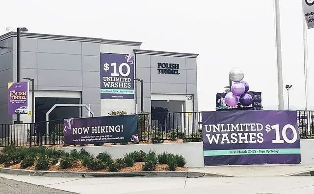 Car wash building with $10 unlimited washes signs and “Now Hiring” banner