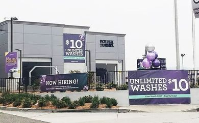 Car wash building with $10 unlimited washes signs and “Now Hiring” banner