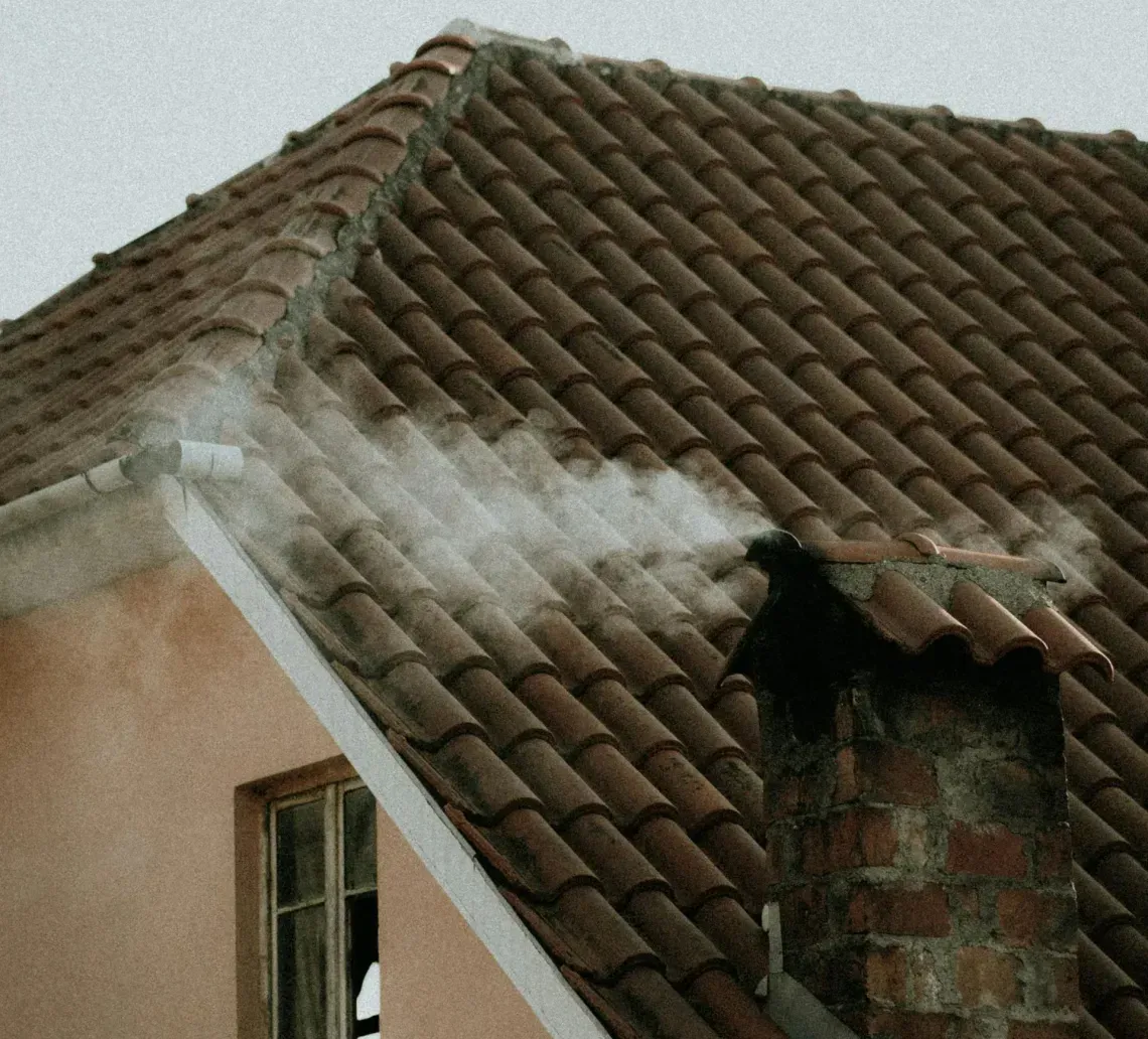 A section of a peach-colored building with a brown tiled roof, featuring a broken window and a damaged roof section.