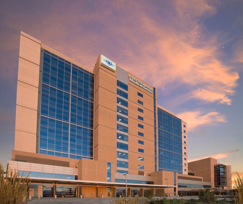Modern tan-and-blue hotel or office building at sunset under a pink-orange sky