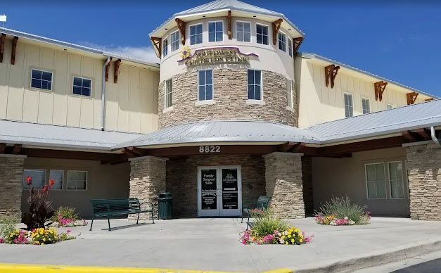 Front entrance of a beige building with stone accents, covered walkway, and flower beds by the doors