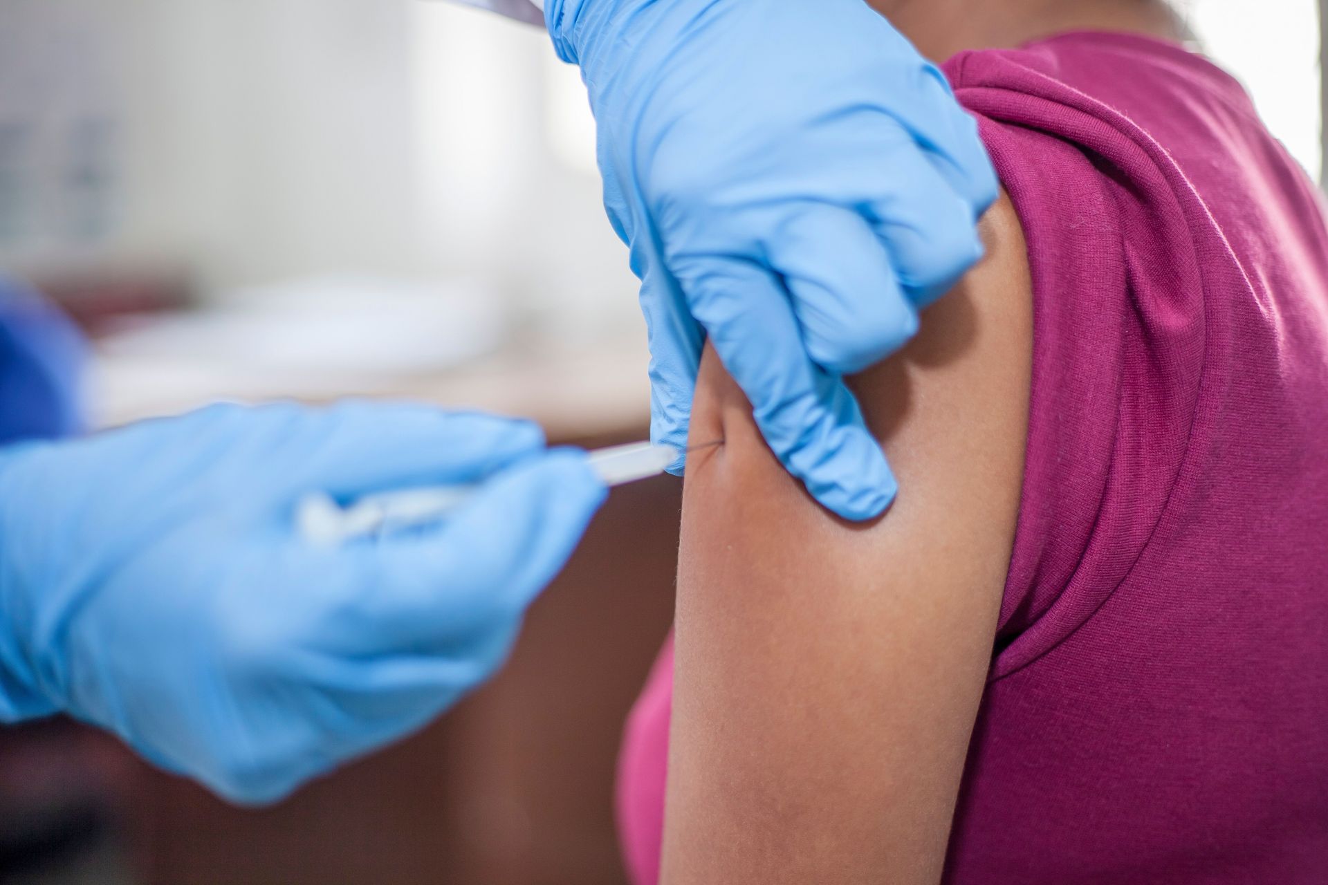 Gloved hands giving an injection into a person’s upper arm