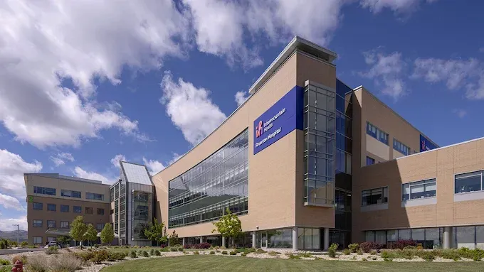 Modern campus building with beige walls, glass facade, and blue signage under a partly cloudy sky