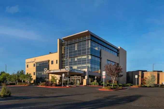 Modern office building with glass facade and beige exterior in a parking lot under a blue sky