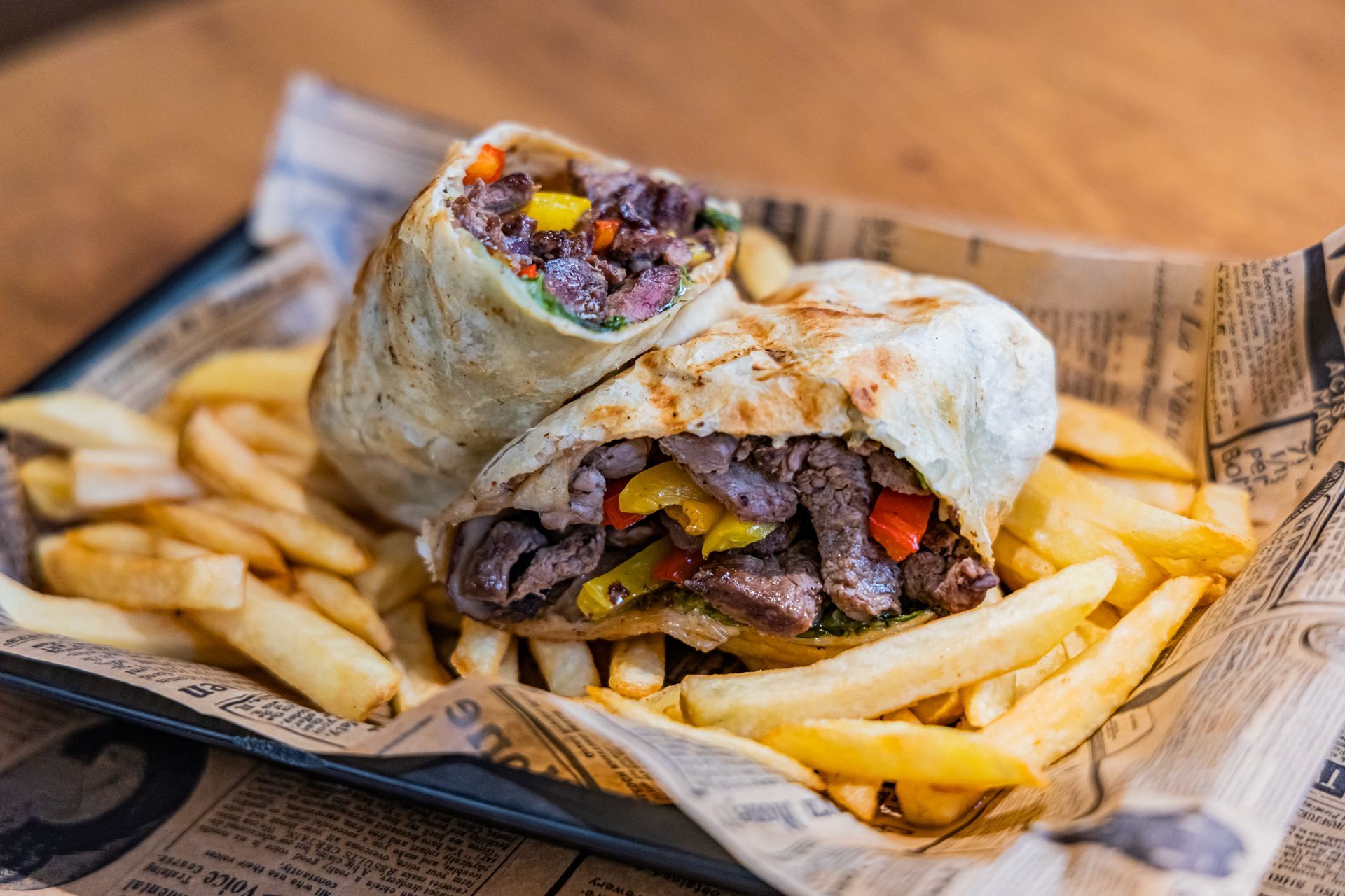 A wrap sandwich is sitting on top of a tray of french fries.
