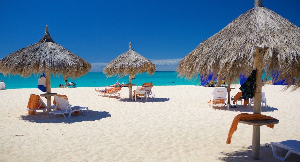 Two lounge chairs under an umbrella on a beach.