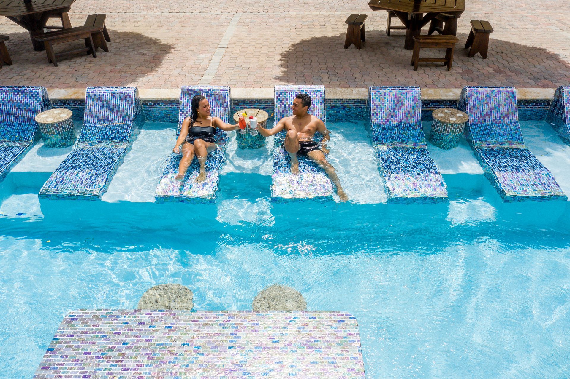 A man and a woman are sitting on lounge chairs in a swimming pool.