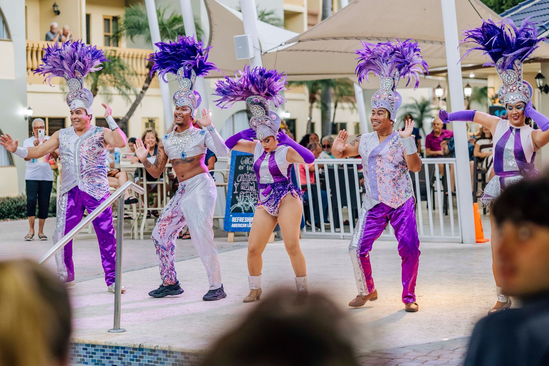 Dancers in purple and silver costumes with large feathered headdresses performing outdoors at a resort.