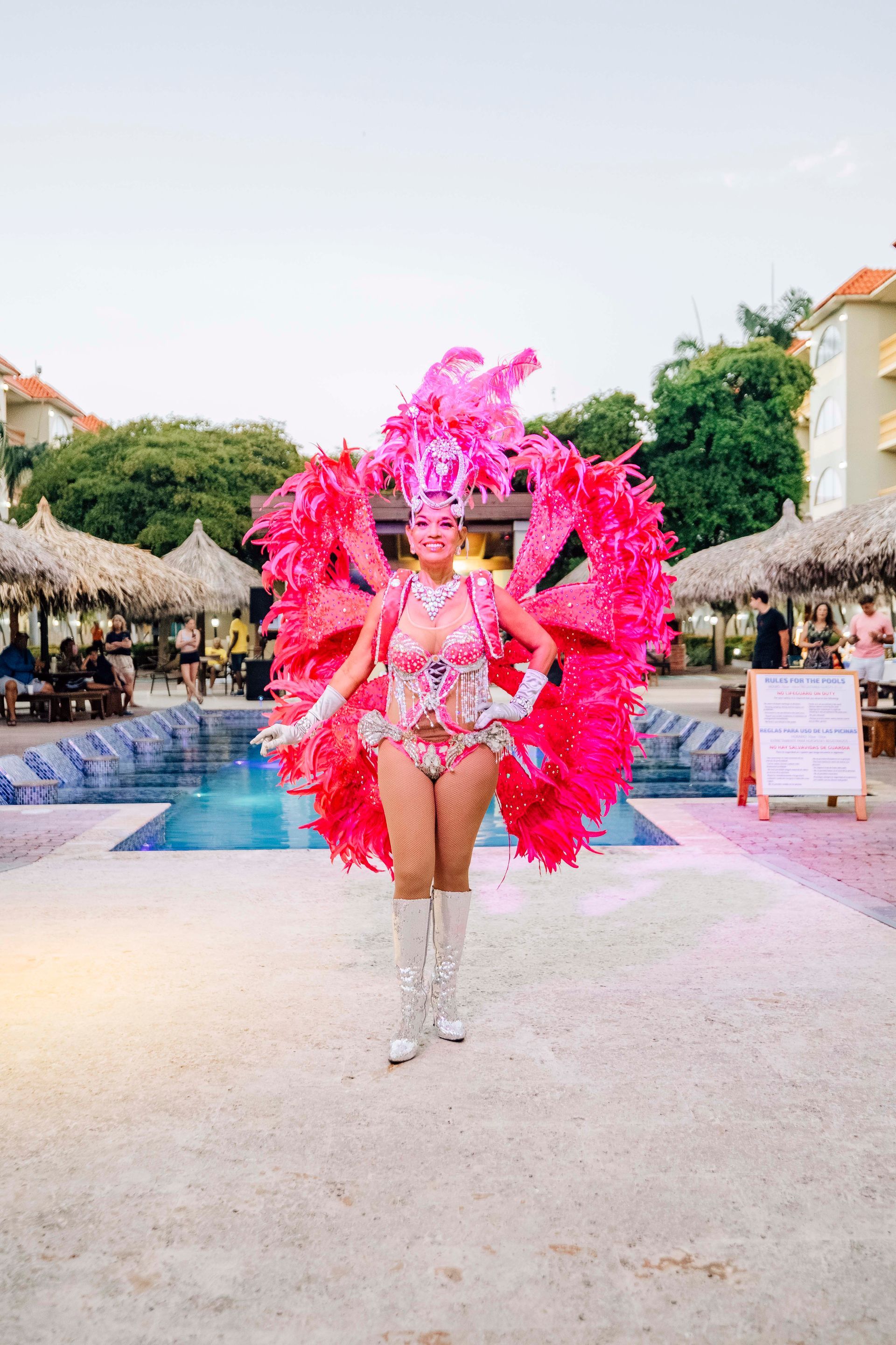 Woman in vibrant pink costume, boots, and headpiece, near a pool.