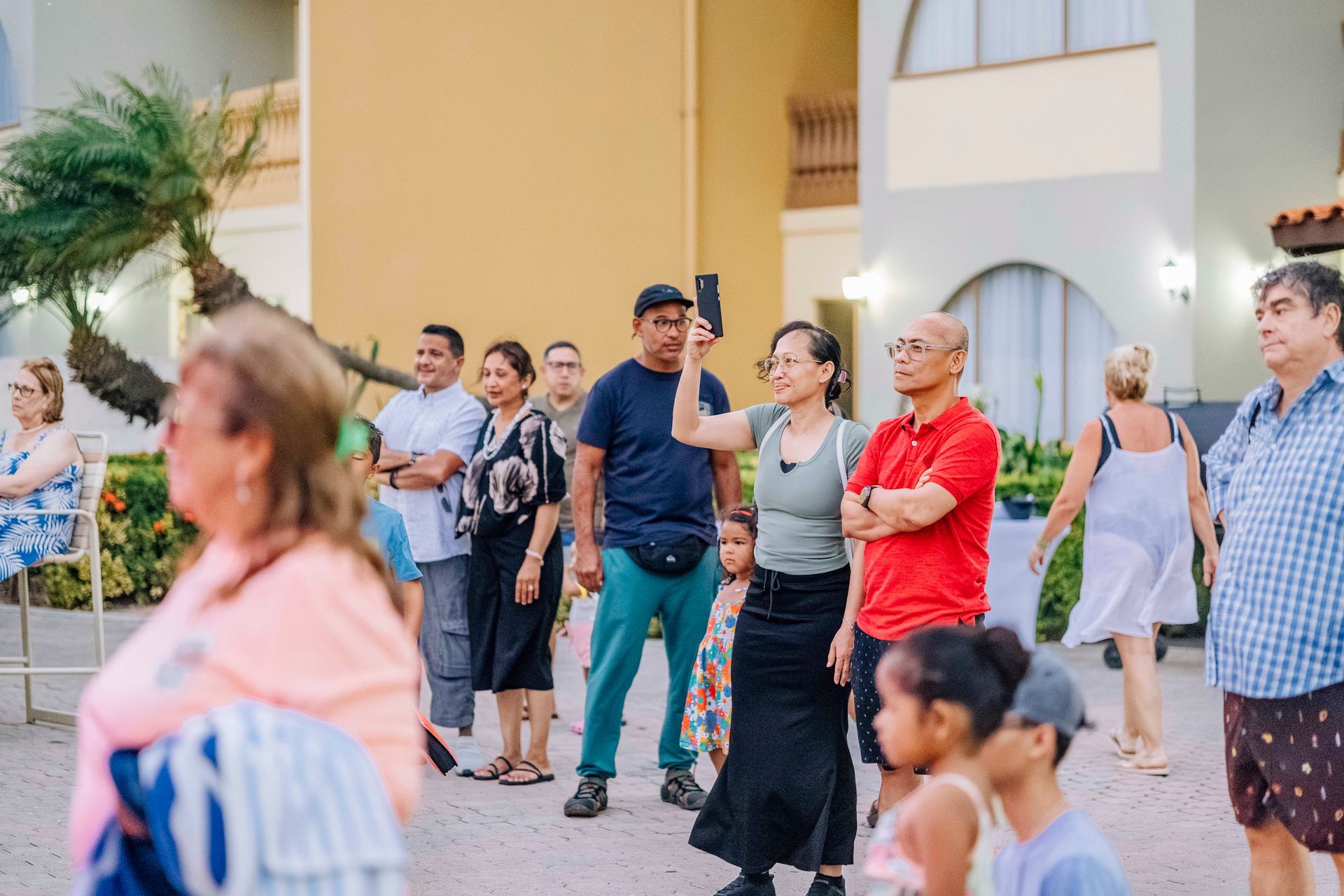 A group of people outdoors, some looking at a phone, near a building.