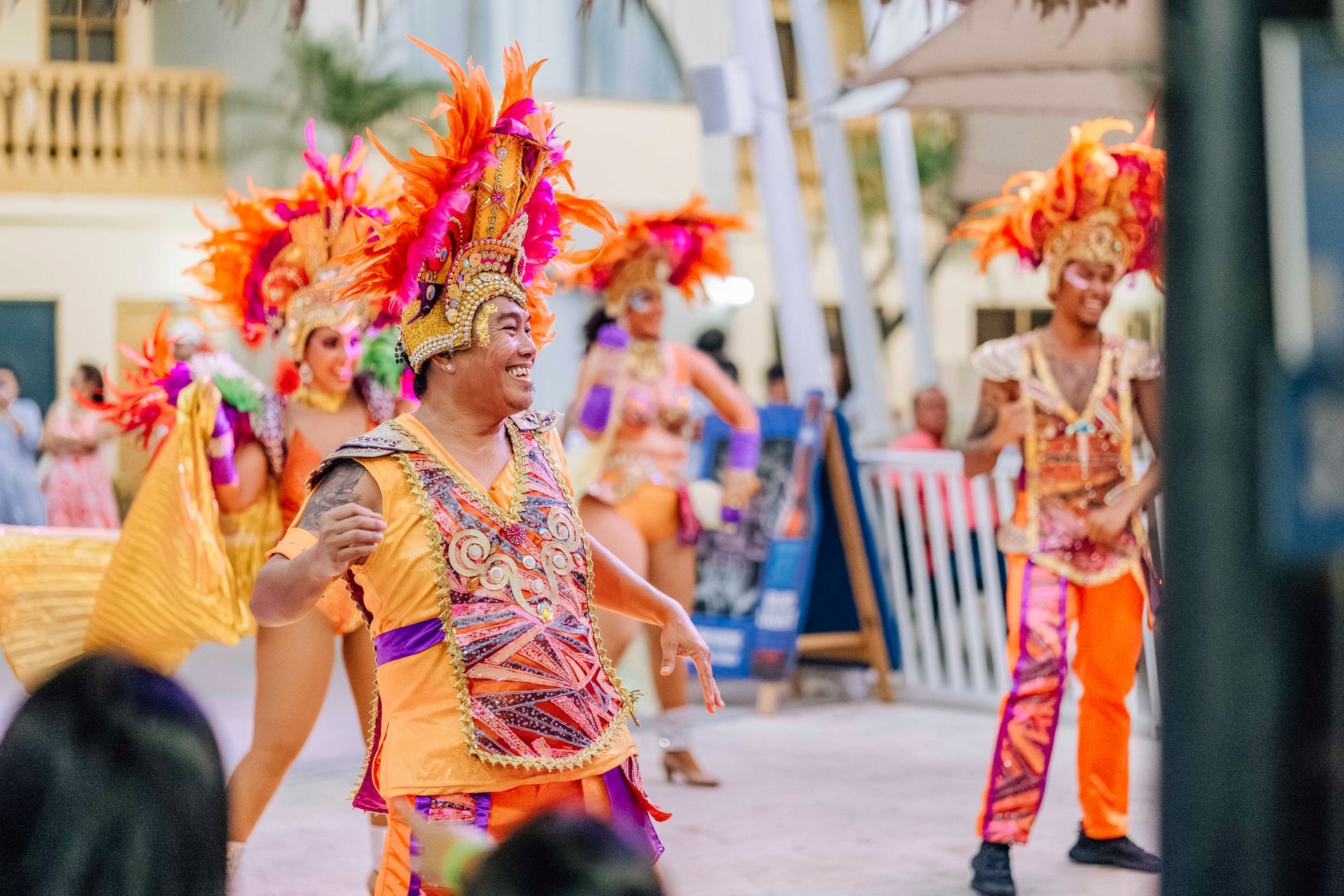 People in vibrant costumes, feather headdresses, dancing in a festive outdoor setting.