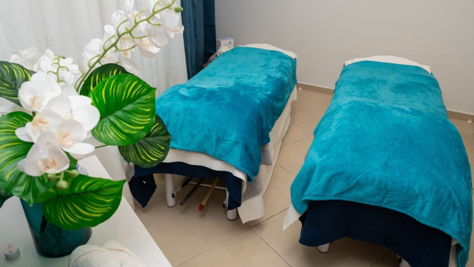 Two massage tables are covered in blue blankets in a room.