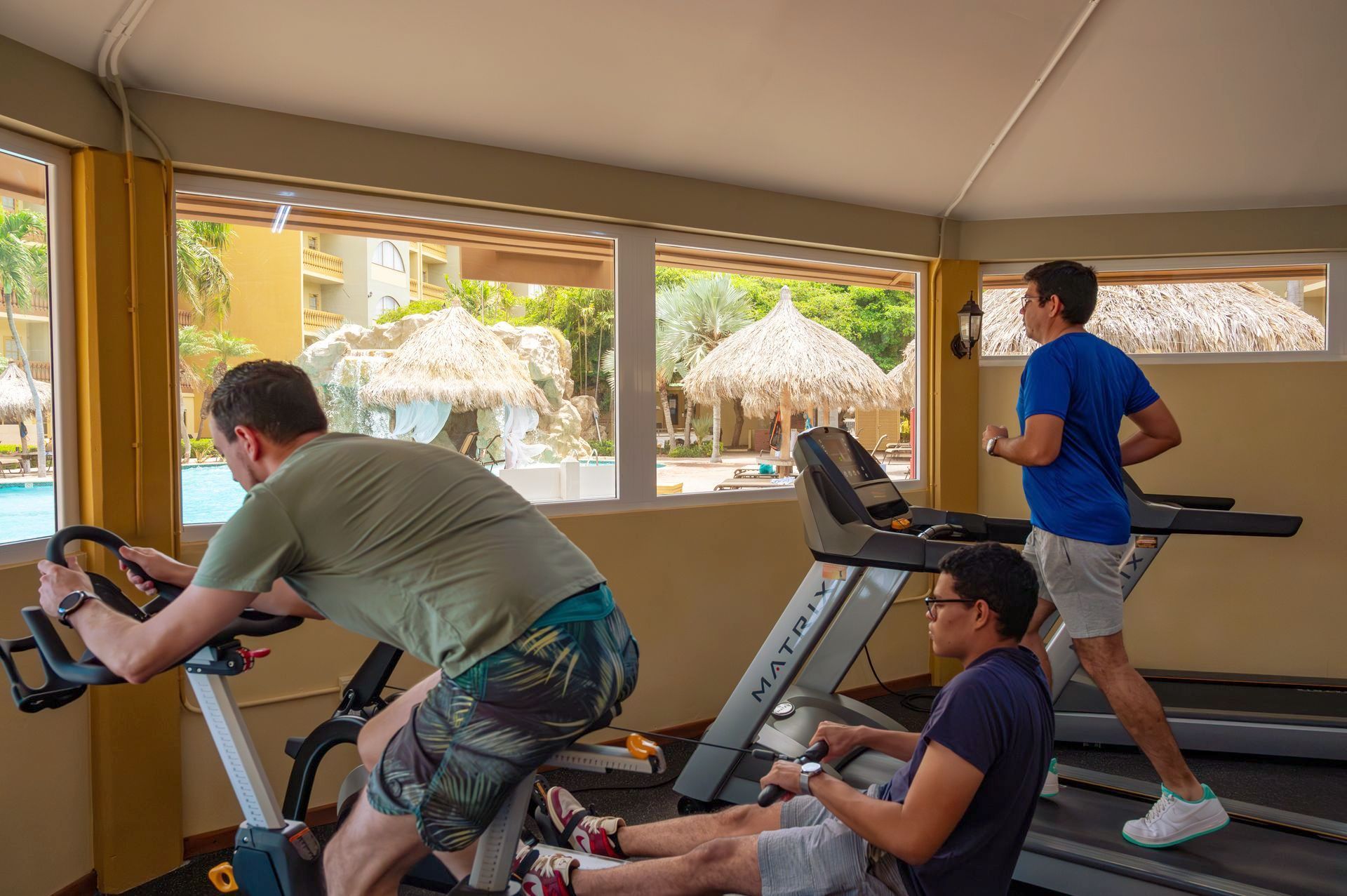 A man is riding an exercise bike in a gym while another man is running on a treadmill.
